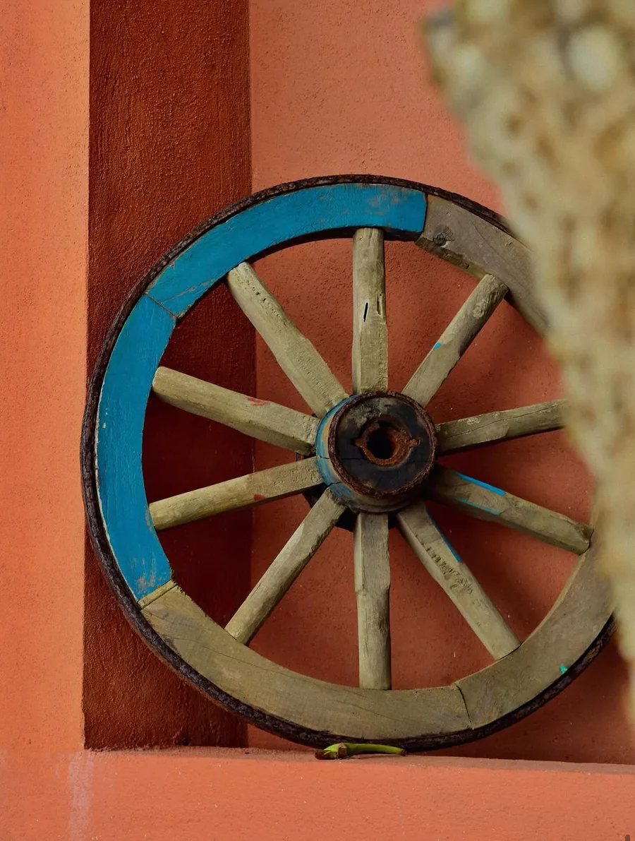 A wooden cart wheel painted blue, leaning against a terracotta wall.